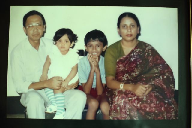 Retrato dde família mostra um homem adulto de roupas brancas, uma mulher com roupas tradicionais do Bangladesh e duas crianças, um menino e uma menina - que está sentada no colo do pai