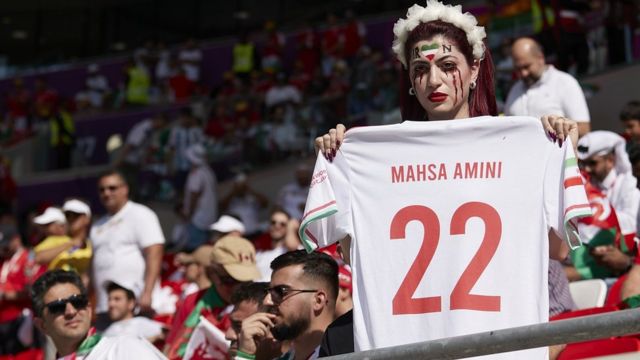 Una aficionada al fútbol iraní sostiene una camiseta de fútbol con el nombre 'Mahsa Amini'.