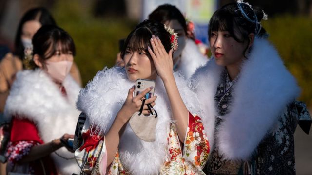 Japonesas vestidas al modo tradicional, con kimono y una pieza de abrigo por encima, caminan con sus celulares en la mano.
