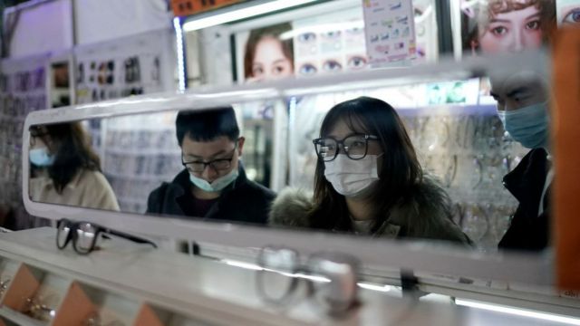 Customers looking in the mirror at a eyewear store at a night market in Wuhan, Hubei Province