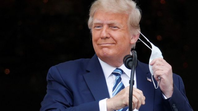 US President Donald Trump removes his mask as he steps out onto a White House balcony to speak to supporters gathered on the South Lawn for a campaign rally the White House is calling 