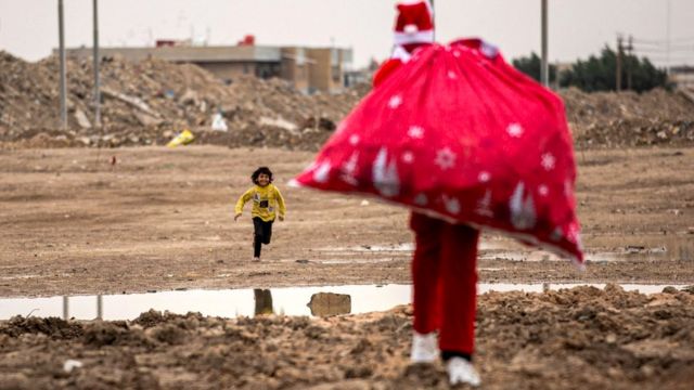 A child runs towards a man as he walks with a sack of gifts dressed as Saint Nicholas (Santa Claus) in a slum near the centre of Iraq's southern city of Basra, 24 December 2021