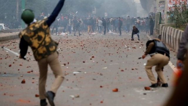 A riot police officer throws a piece of brick towards demonstrators during a protest against a new citizenship law in Seelampur, Delhi
