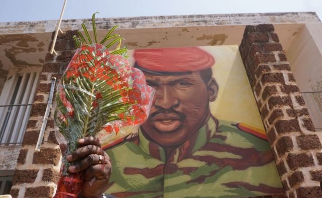 A man holds flowers next to an image of Thomas Sankara, in front of the headquarters of the National Council of the Revolution (CNR), in Ouagadougou in 2019. The former leader was killed at the site in 1987.