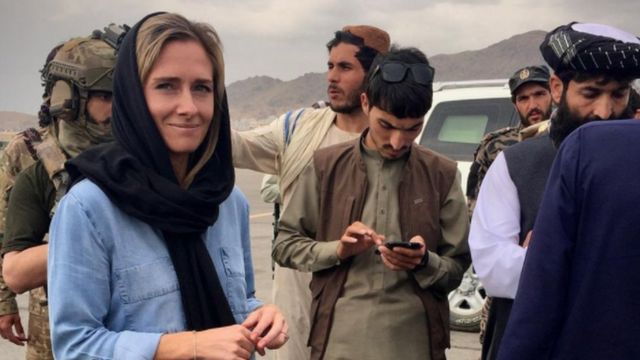 A jornalista Charlotte Bellis, uma mulher branca com hijab, ao lado de oficiais do Talebã no Afeganistão