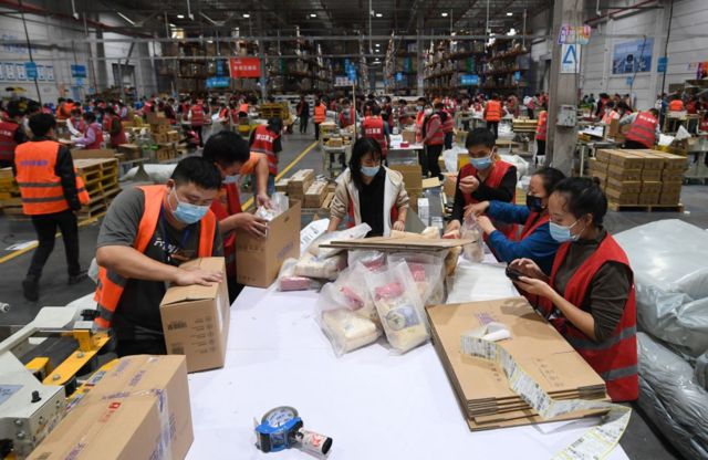 Работниуи пакуют посылки в помещении большого склада