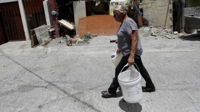 Uma mulher idosa carrega dois baldes de água