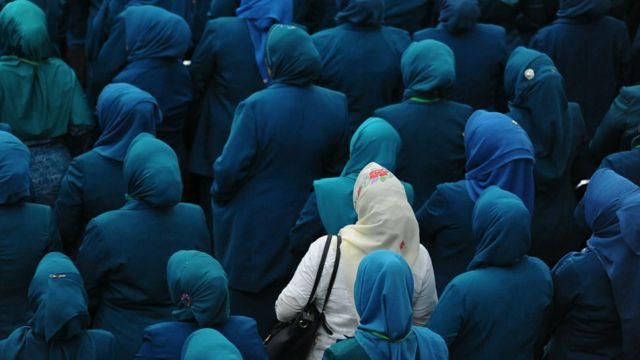 General view of women wearing dark blue Hijabs, except for one who wears white and looks different from the rest