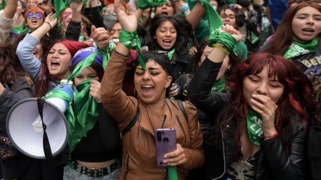 Várias mulheres erguendo os braços, gritando e sorrindo em comemoração