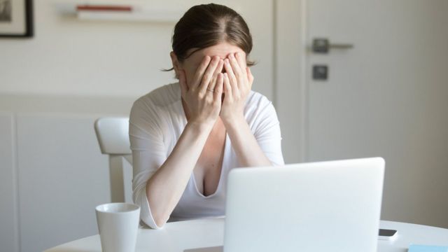 Woman working at desk with laptop, hands closing face