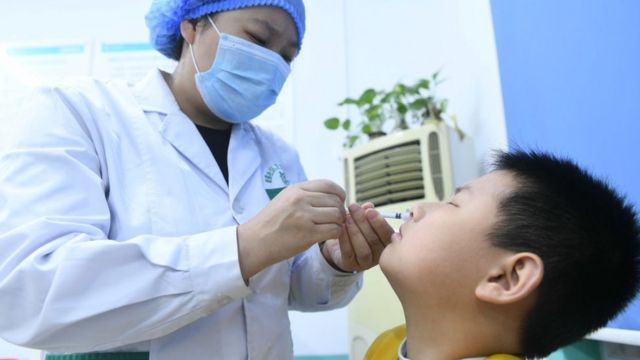 Una enfermera aplica vacuna nasal a un niño en China
