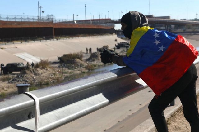 Wrapped in the Venezuelan flag, Alejandro Rojas, a 22-year-old Venezuelan migrant, looks toward the United States from across the border fence, in Ciudad Juárez, Chihuahua, Mexico, on December 20, 2022.