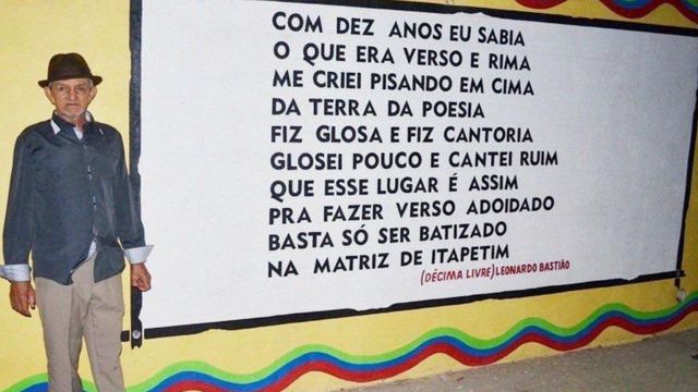 Bastião posa ao lado de seu poema registrado em um muro