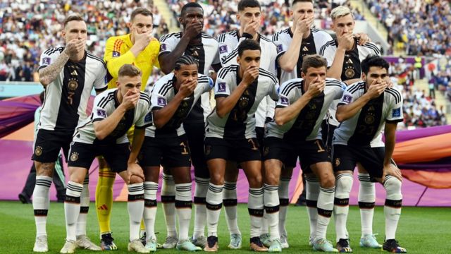 Jogadores posando para foto, no gramado, com mão na boca