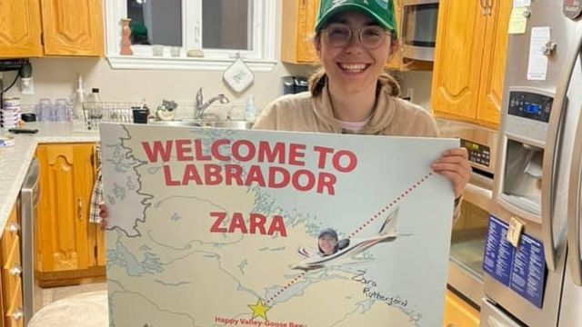 Zara Rutherford de pie en una cocina con un cartel que dice Bienvenida a Labrador, Zara.