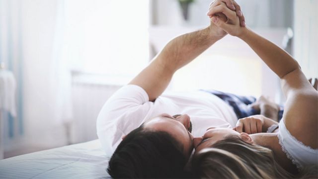 Una pareja acostada en una cama sujetándose las manos.