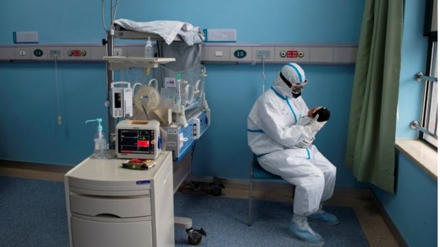 Profissional inteiramente paramentado segura bebe em sala de hospital, com vários aparelhos ao lado