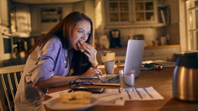 yemek yiyerek bilgisayarda çalışan kadın