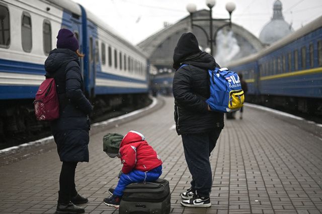 اثنان من النازحين وطفل صغير يجلس فوق حقيبة سفر، بانتظار ركوب قطار من مدينة لفيف في غرب أوكرانيا إلى رومانيا، في الخامس من مارس/آذار 2022