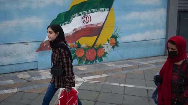 Women walk past an Iran flag in downtown Tehran