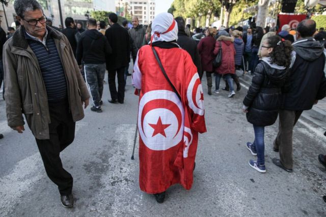 Une femme drapée dans le drapeau national marche sur une route à l'occasion de l'anniversaire du printemps arabe 2011.