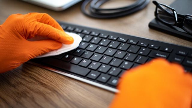 Mão limpando teclado em escritório