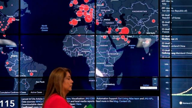 Mujer pasa caminando frente al mapa de los casos de coronavirus en el mundo.