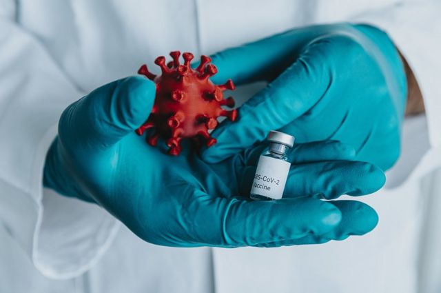 Uma pessoa com luvas carrega uma vacina e um modelo de um coronavírus