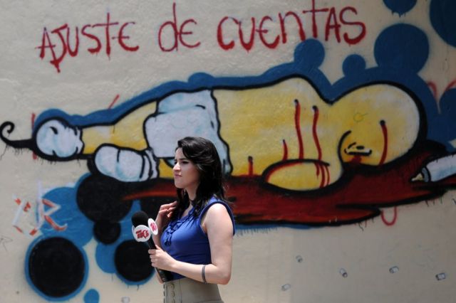 Periodista frente a un grafiti en el que se lee "Ajuste de cuentas" el 26 de abril de 2013.