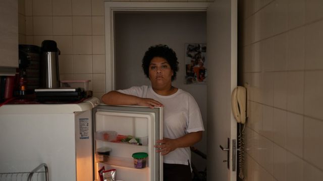 Franciele abre sua geladeira, com feição séria olhando para a câmera