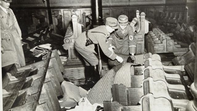 Soldados nazistas despejando gasolina em bancos de uma sinagoga