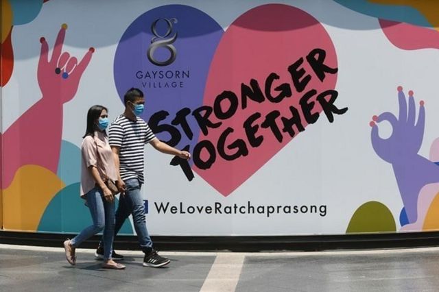 ภาพคนเดินหน้าป้ายที่เขียนว่า strong together