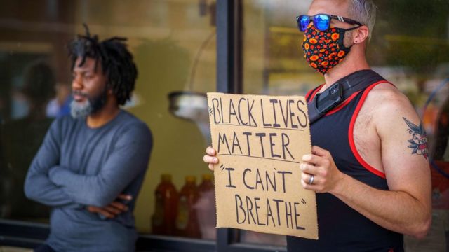 Un hombre blanco sosteniendo un cartel que dice "Las vidas negras importan. No puedo respirar".