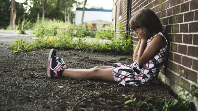 Child with her head in her hands sitting on the ground