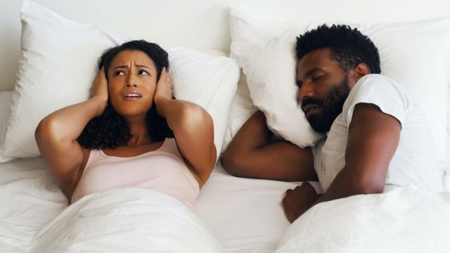 Woman covering her ears in bed as her partner next to her snores