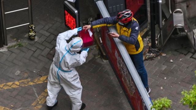 A worker in protective gear (left) receives an item from a delivery man at the entrance of a housing complex during the second stage of the pandemic lockdown in Shanghai's Jing'an district.