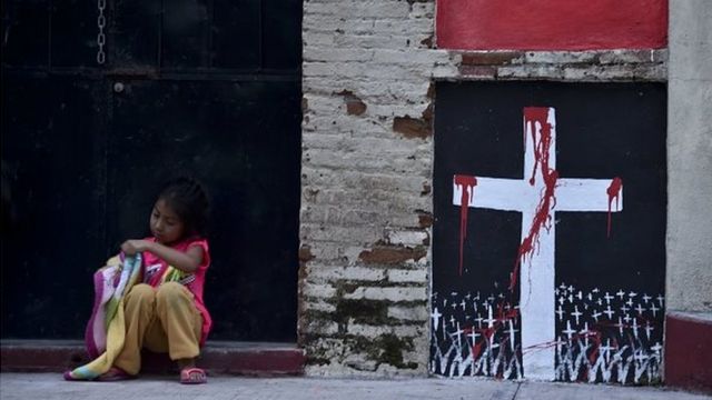 Uma menina senta-se ao lado de um mural com uma cruz coberta de sangue em 30 de setembro de 2014, durante o velório do estudante Julio Cesar Ramirez Nava que foi morto em Iguala,