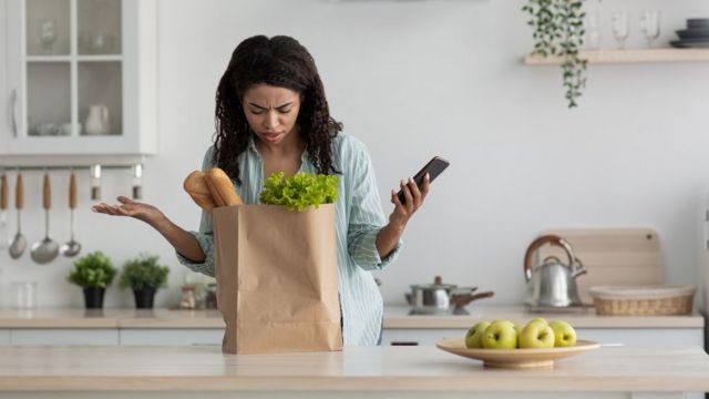 Una mujer mira desconcertada una bolsa von productos comestibles.