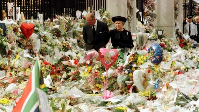 戴安娜巴黎车祸殒命，英国民众在白金汉宫前摆放了无数鲜花致哀。女王伊丽莎白二世最初的反应受到批评，后来她的态度明显转变，王室与公众之间的紧张后来随时间推移逐渐消退。图为女王夫妇在王宫门外(photo:BBC)