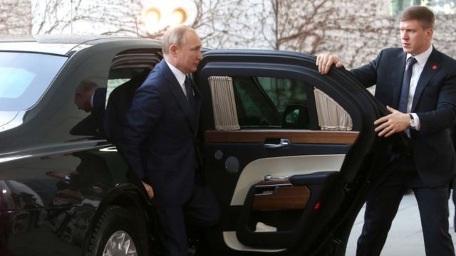 Vladimir Poutine sort d'une voiture avec son garde du corps.