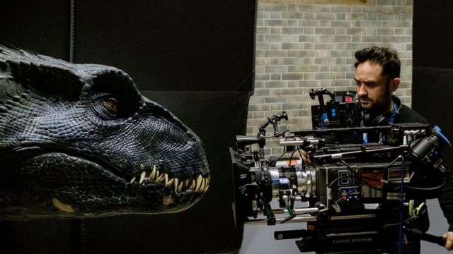 Um cinegrafista segura uma camera apontada para um robô de dinossauro durante a filmagem do longa 'Jurassic World: Reino Ameaçado'