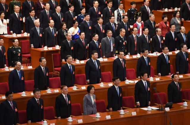 Chinese President Xi Jinping, center, sings the national anthem with other leaders at the closing session of the National People's Congress in Beijing on March 15, 2019.  - From left to right in the second row are Vice President Wang Qishan, Politburo Standing Committee Member Zhao Leji, Standing Committee Member Wang Yang, President Xi Jinping, Premier Li Keqiang, Politburo Standing Committee Member Wang Huning, Standing Committee Member Han Zheng, and Standing Committee Member Ding Xuexiang.