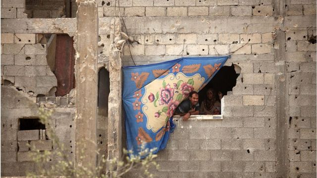 مواطن من غزة ينطر من خلال فتحة في جدار بيته الذي دمرته الصواريخ الإسرائلية