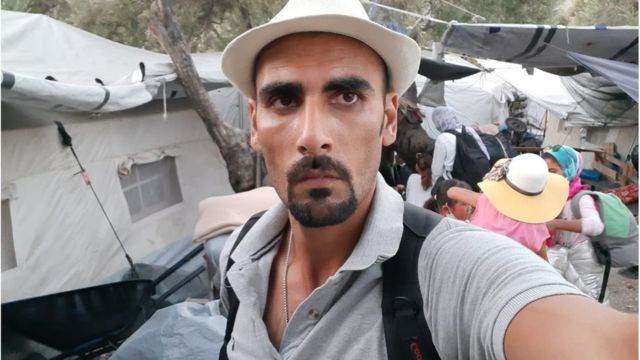 A photo of Talibshah Hosseini standing beside their new shared tent in Moria camp before the fire