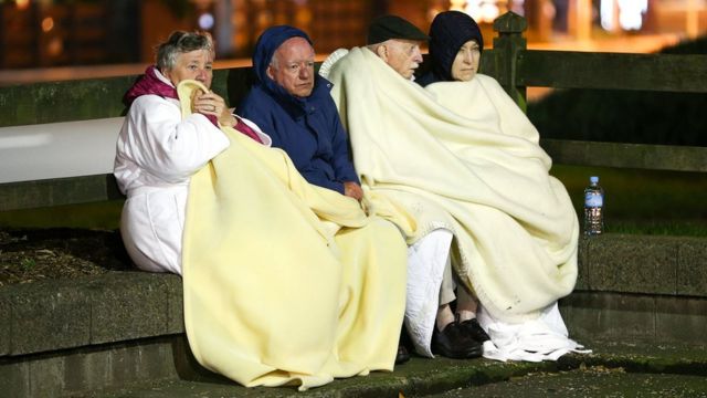 Four people sit on a low wall under blankets after the earthquake