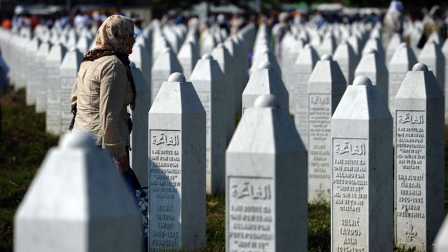 Mujer caminando frente a filas interminables de lápidas con los nombres de las víctimas de Srebrenica