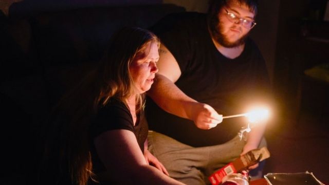 Um homem e uma mulher acendem velas no escuro
