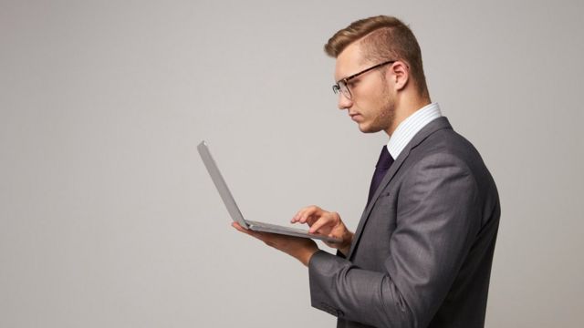 Un ejecutivo de pie, escribiendo en su laptop