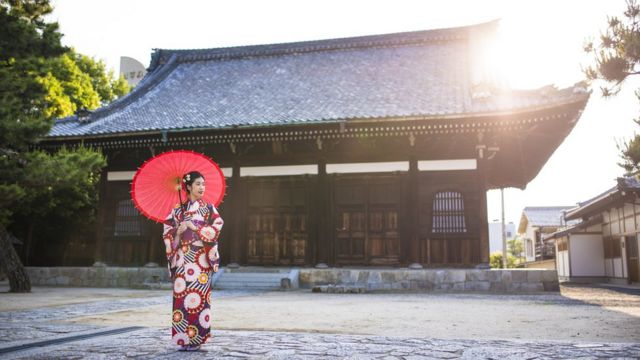 A woman stands in traditional clothing outside a Japanese temple