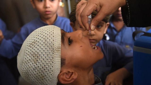 عامل صحي يعطي لقاح شلل الأطفال لصبي صغير في مدرسة في كراتشي